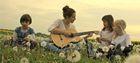 Symbolfoto: Gitarrenlehrerin mit Kindern auf einer Wiese