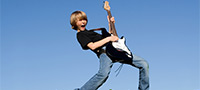 Symbolfoto: Junge mit E-Gitarre in der Hand auf einer Wiese